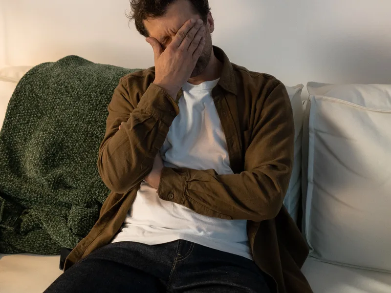 Mann sitzt besorgt auf dem Sofa, Symbol für das ständige Grübeln bei generalisierter Angststörung
